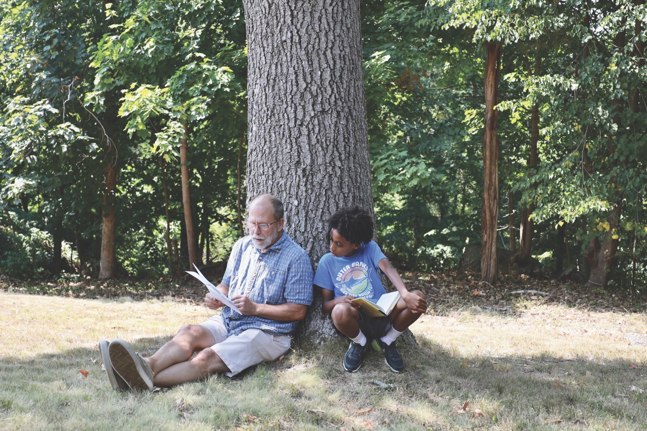 student and teacher reading by tree