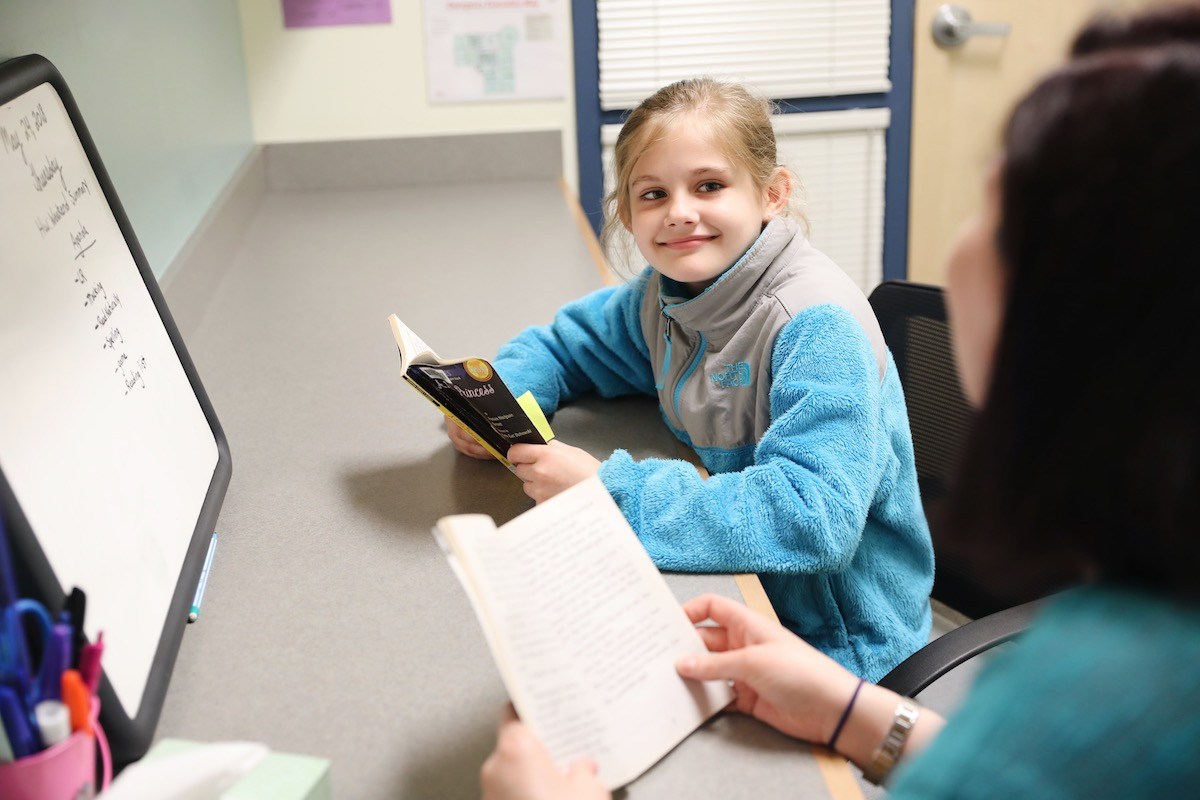 student with book smiling at teacher