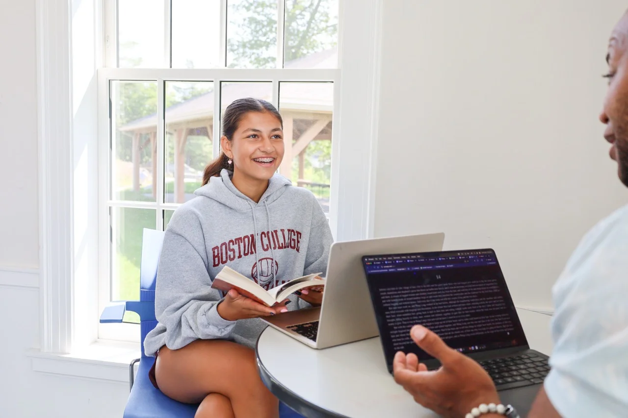 student working with teacher on with book and computer